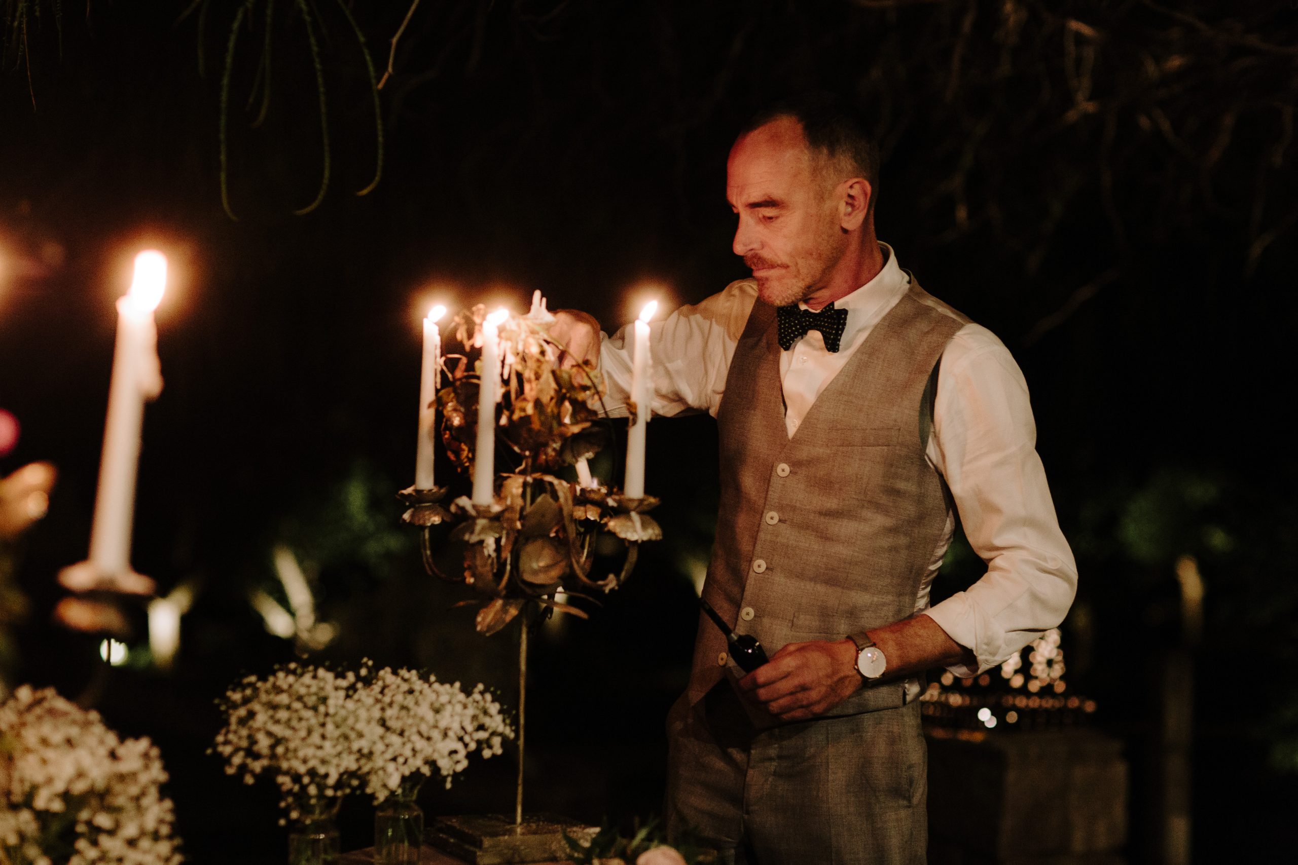 A man in a bow tie sits at a candlelit table