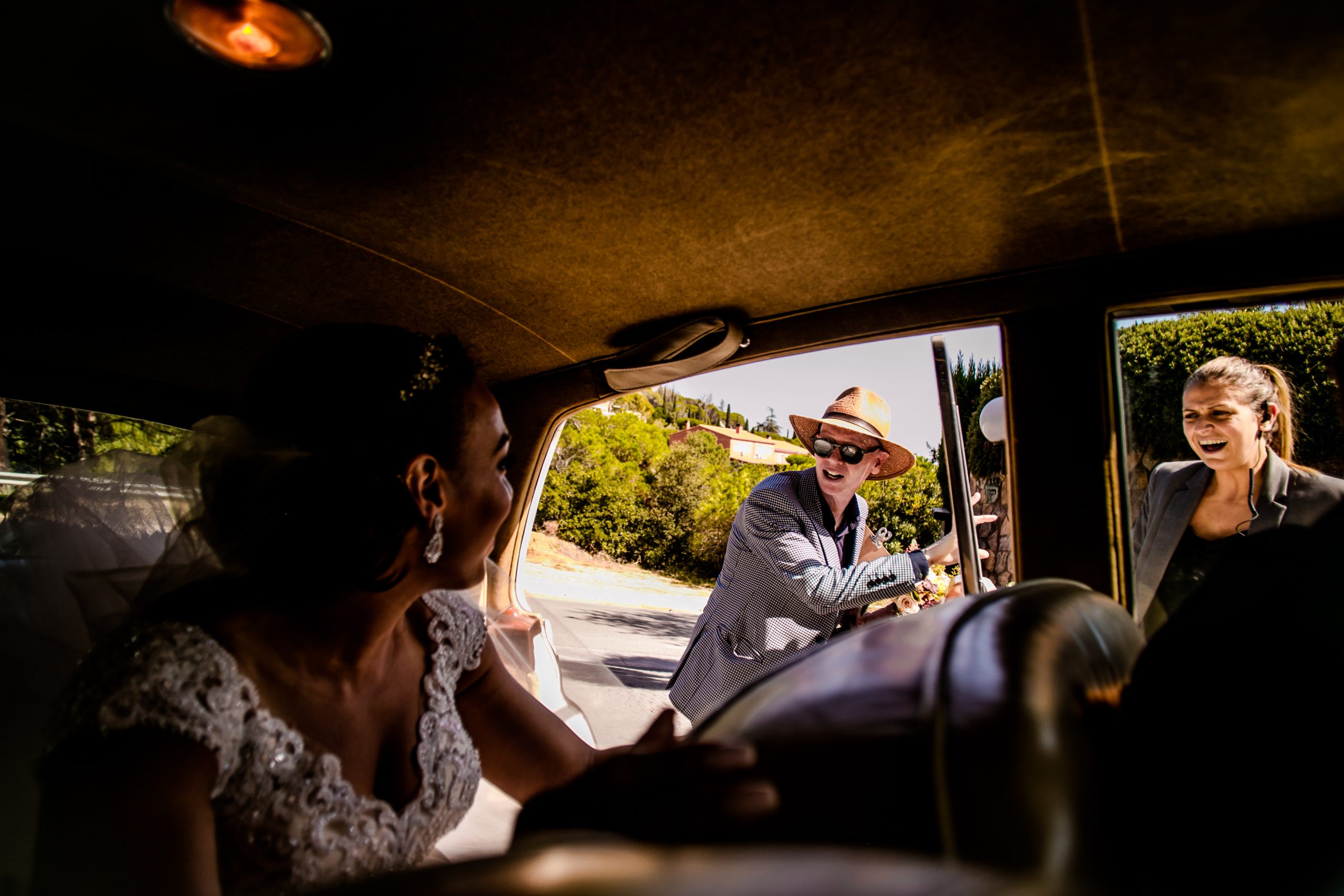 A man in a straw hat greets the bride through the open window of her vintage car