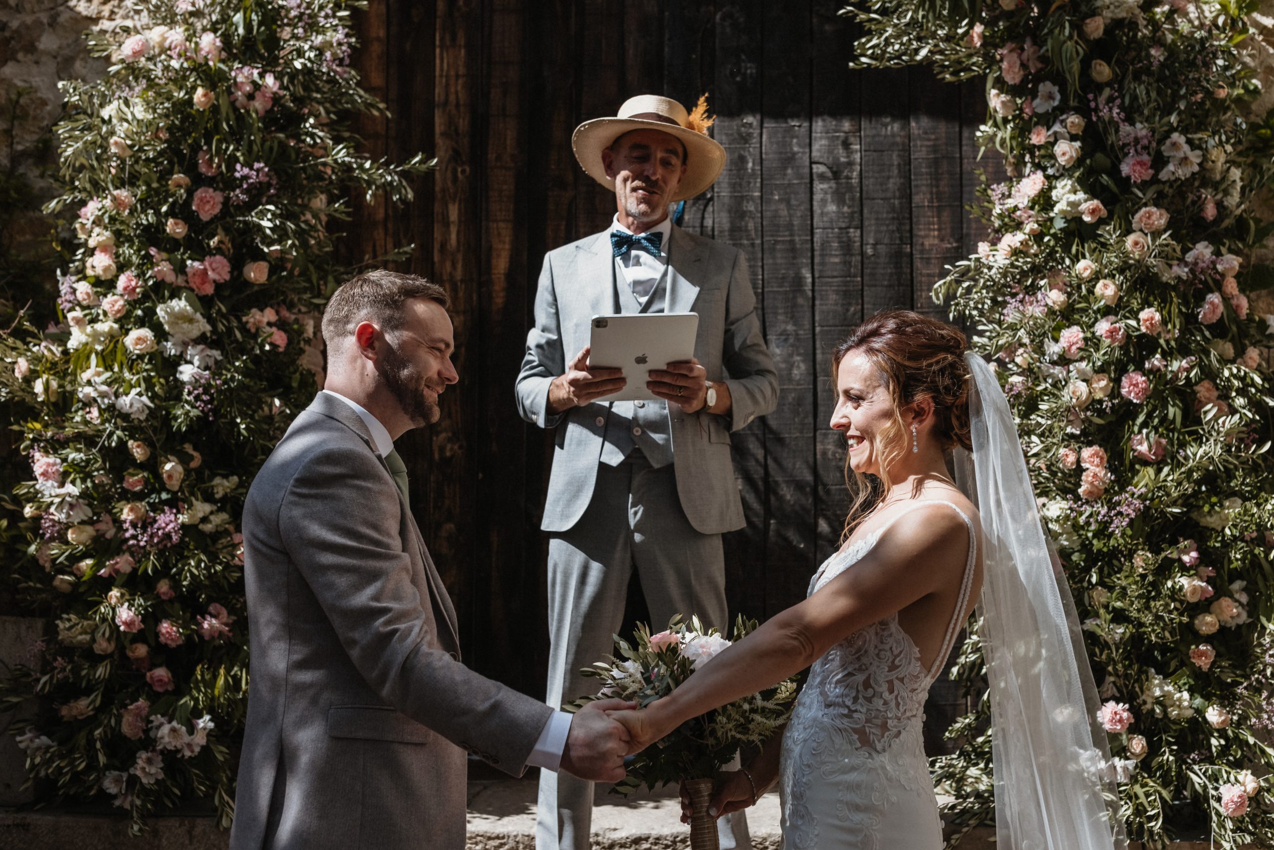 A celebrant reads from a tablet during an outdoor wedding ceremony
