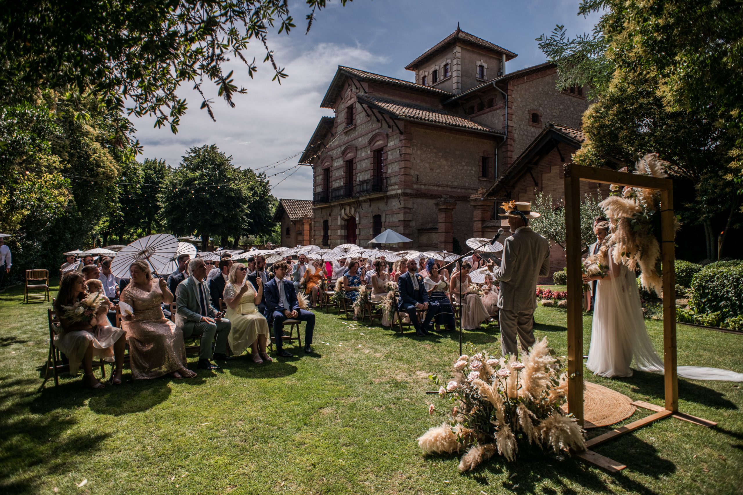 Guests with white parasols gather for an outdoor ceremony at a stone venue