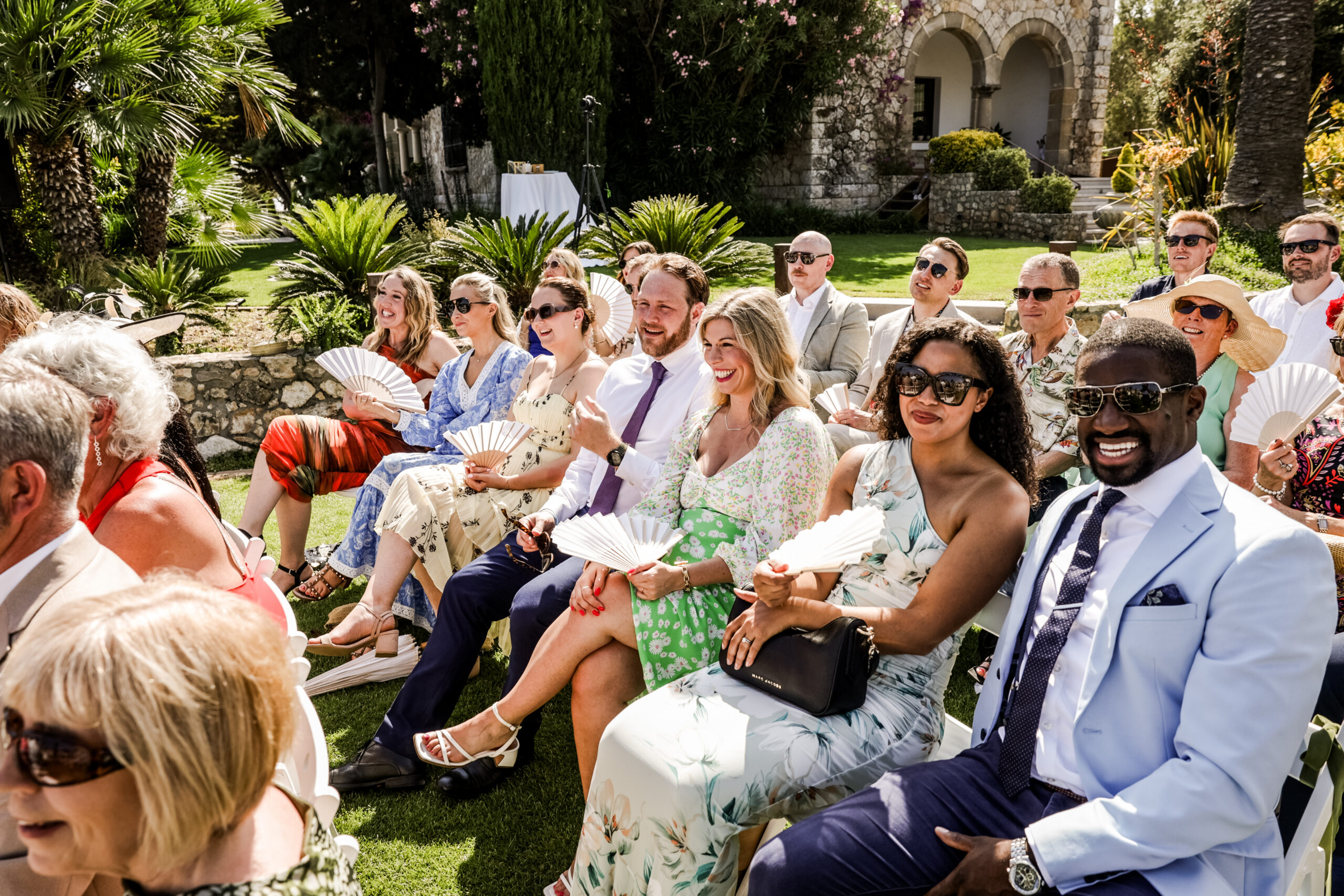 wedding-guests-laughing-during-ceremony-barcelona Wedding guests laughing together during an outdoor ceremony in Barcelona